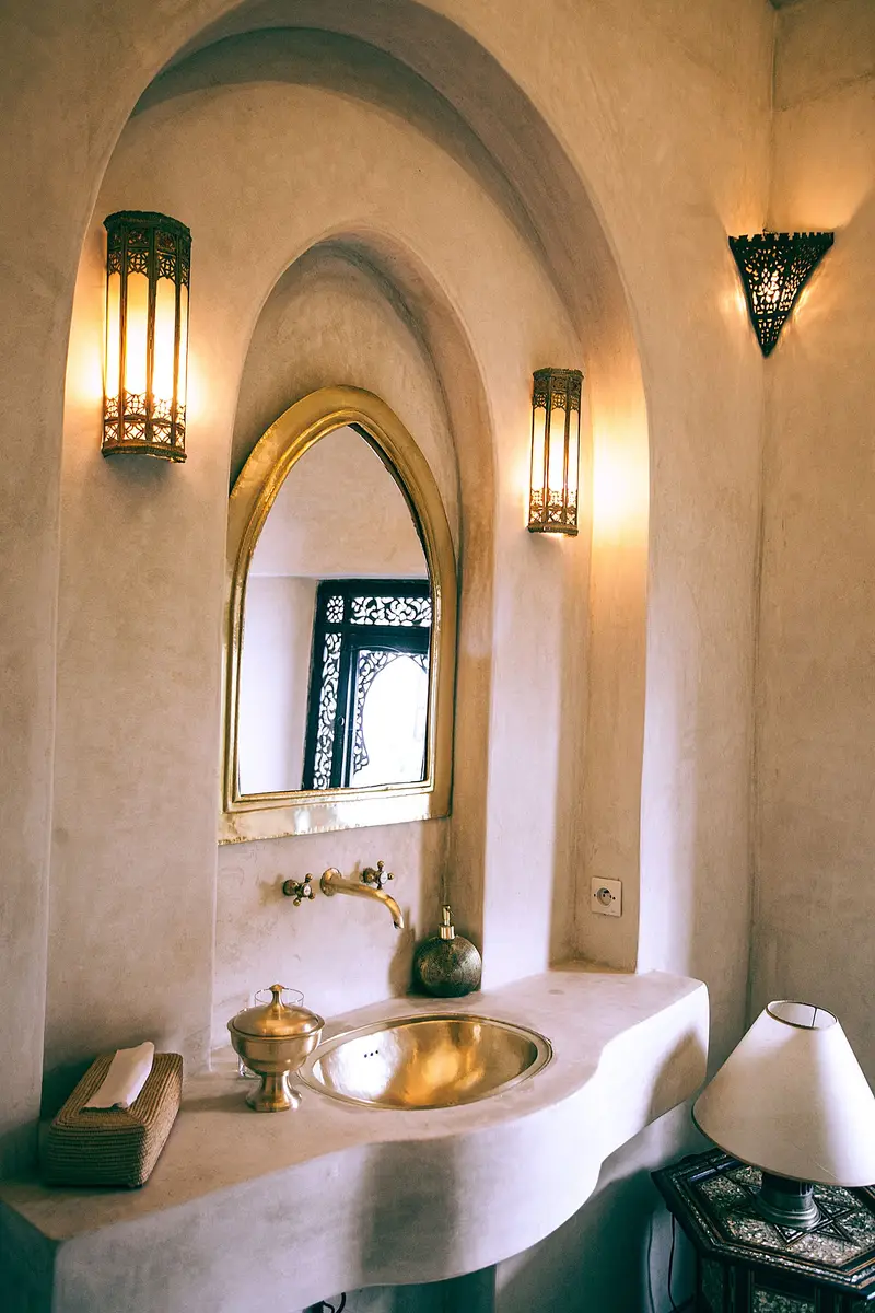 Salle de bain en tadelakt avec miroir doré en arc et appliques