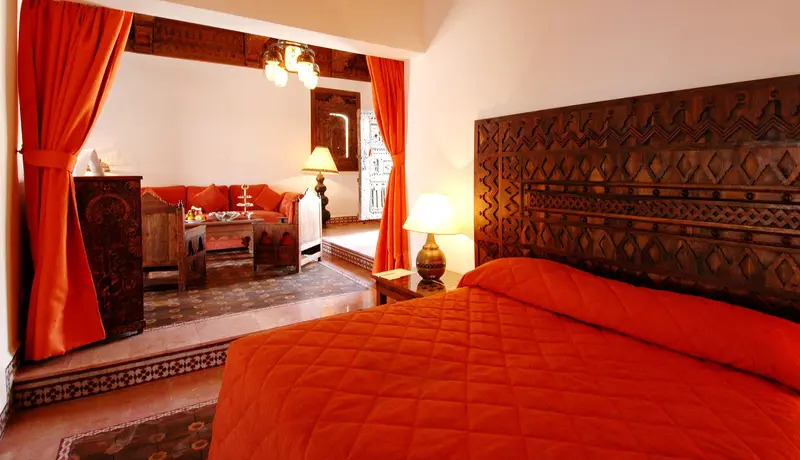 Chambre aux tons safran avec tête de lit sculptée et coin salon
